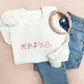 White crewneck sweatshirt styled with jeans a pink headband. The sweatshirt has cute dance icons embroidered across the chest in pink thread.