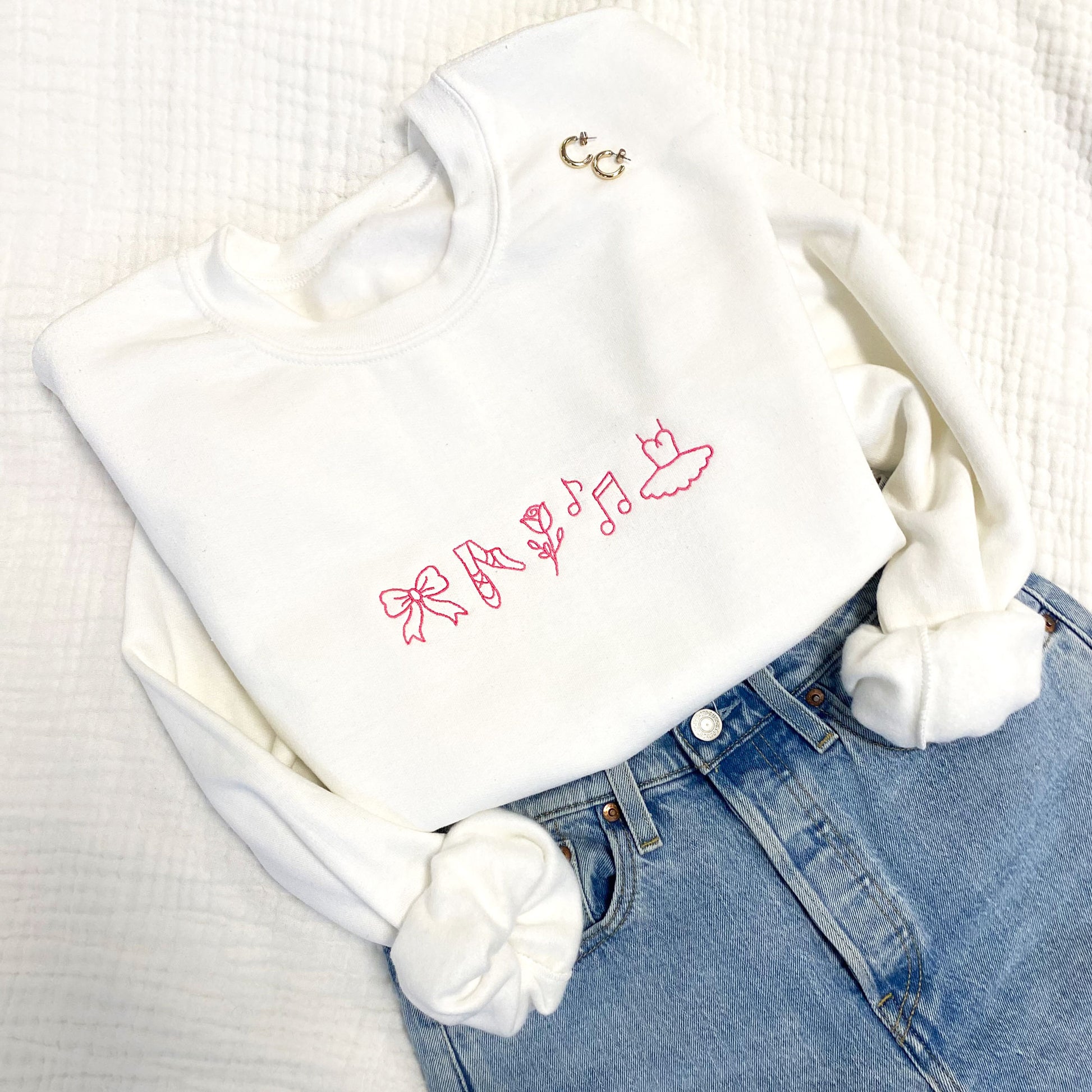 Styled flay lay of an embroidered dance icon crewneck sweatshirt with pink thread.