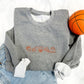 flatlay of graphite heather crewneck sweatshirt with basketball icons embroidered in orange thread