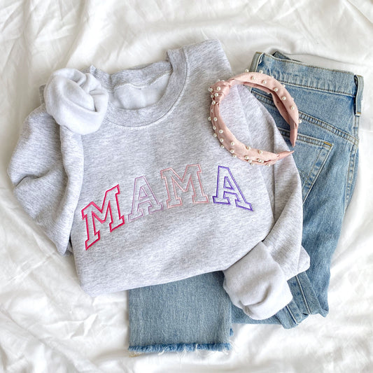 styled flat lay of an ash crewneck sweatshirt with embroidered athletic block mama in alternating shades of pink and purple