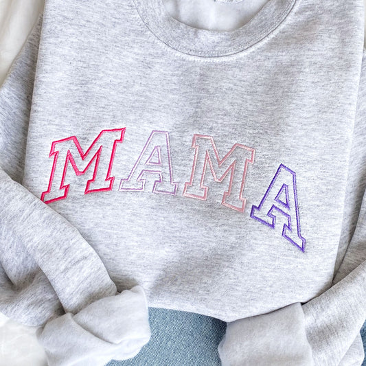 close up of a flat lay of an ash crewneck sweatshirt with embroidered athletic block mama in alternating shades of pink and purple