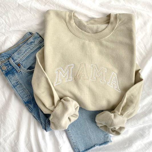 flat lay photo of a sand crewneck sweatshirt with embroidered MAMA in alternating neutral threads across the chest styled with jeans