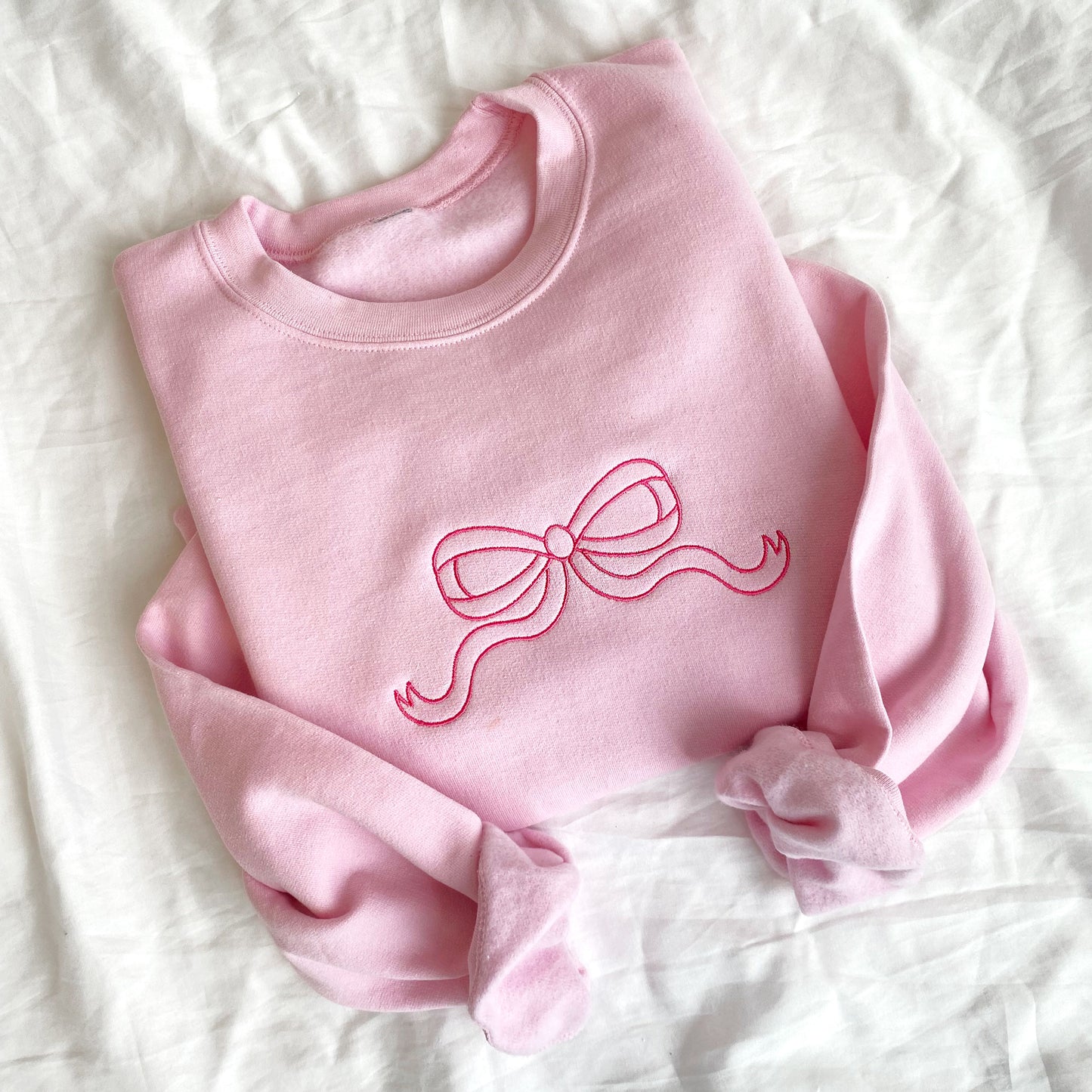flat lay of light pink crewneck sweatshirt with large outlined embroidered pink bow