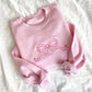 flat lay of light pink crewneck sweatshirt with large outlined embroidered pink bow