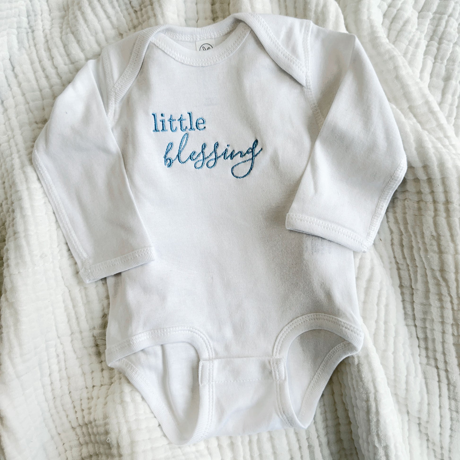 white baby long sleeve bodysuit with a cute little blessings embroidered design on the center chest