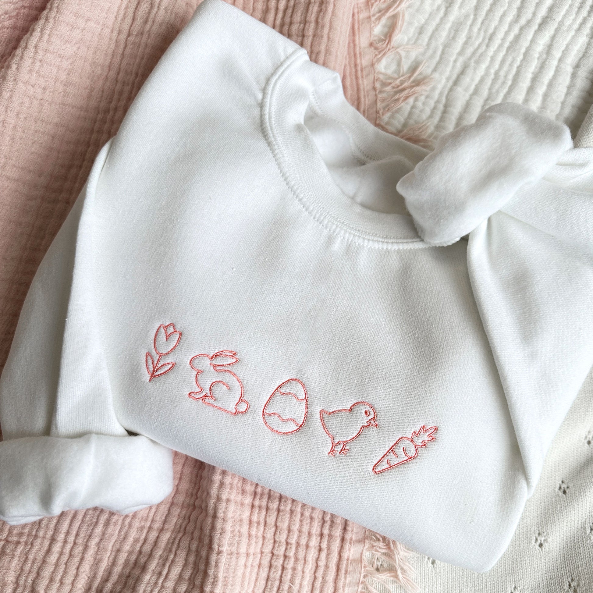 white crewneck sweatshirt with coral pink easter icons embroidered across the chest