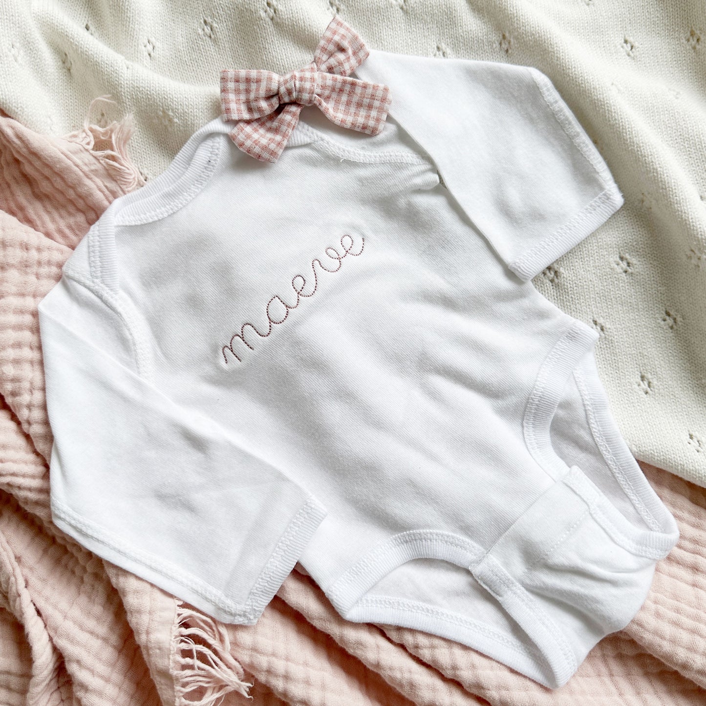 baby bodysuit with a name stitched across the chest in a dark pink thread