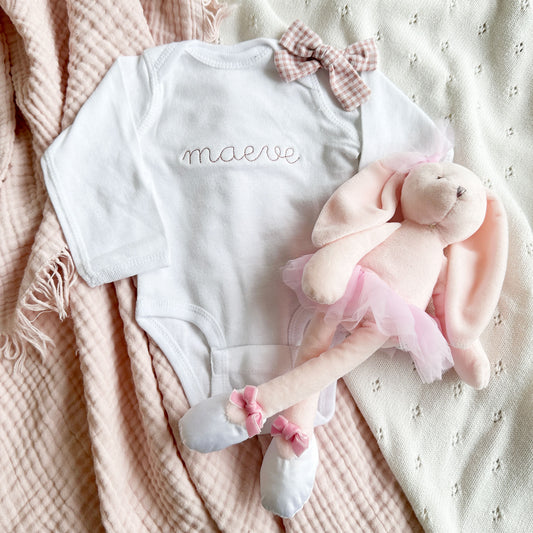 white infant long sleeve bodysuit with a custom name stitched in a delicate font across the chest