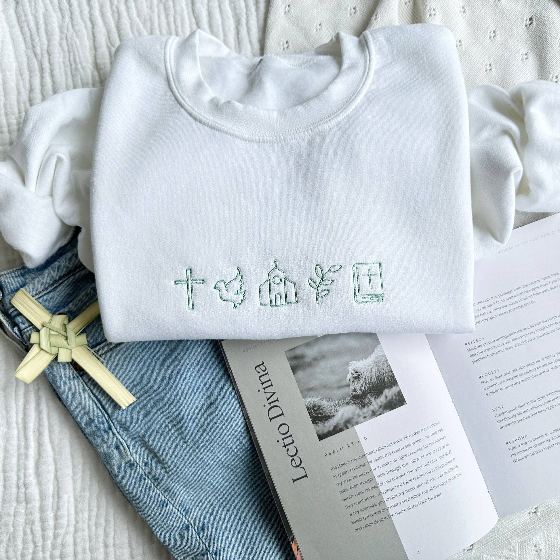 styled flat lay photo of white crewneck sweatshirt with mini religious icons for easter embroidered across the chest