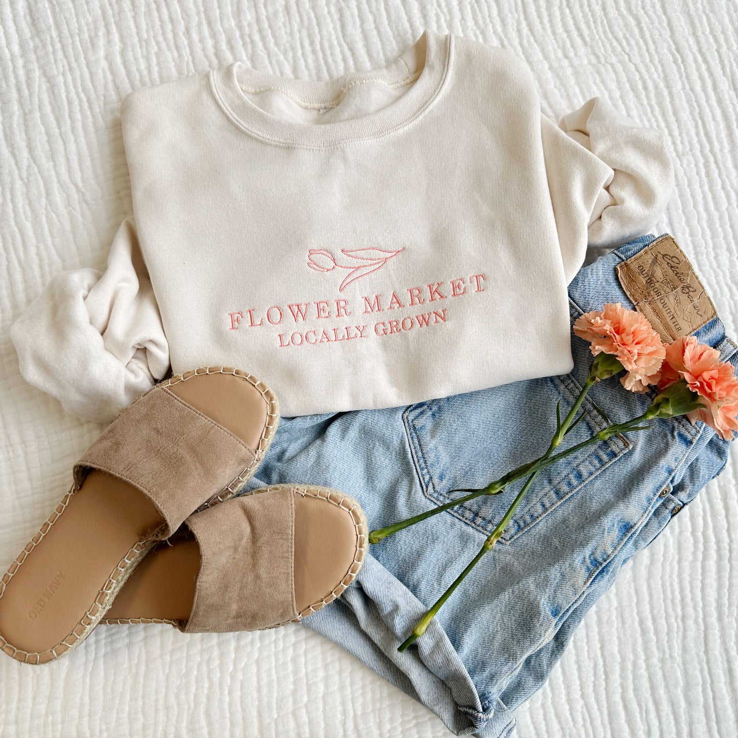 jean shorts, flowers, and sandals styled with a sweet cream crewneck sweatshirt with aflower market and tulip embroidered coral pink design 
