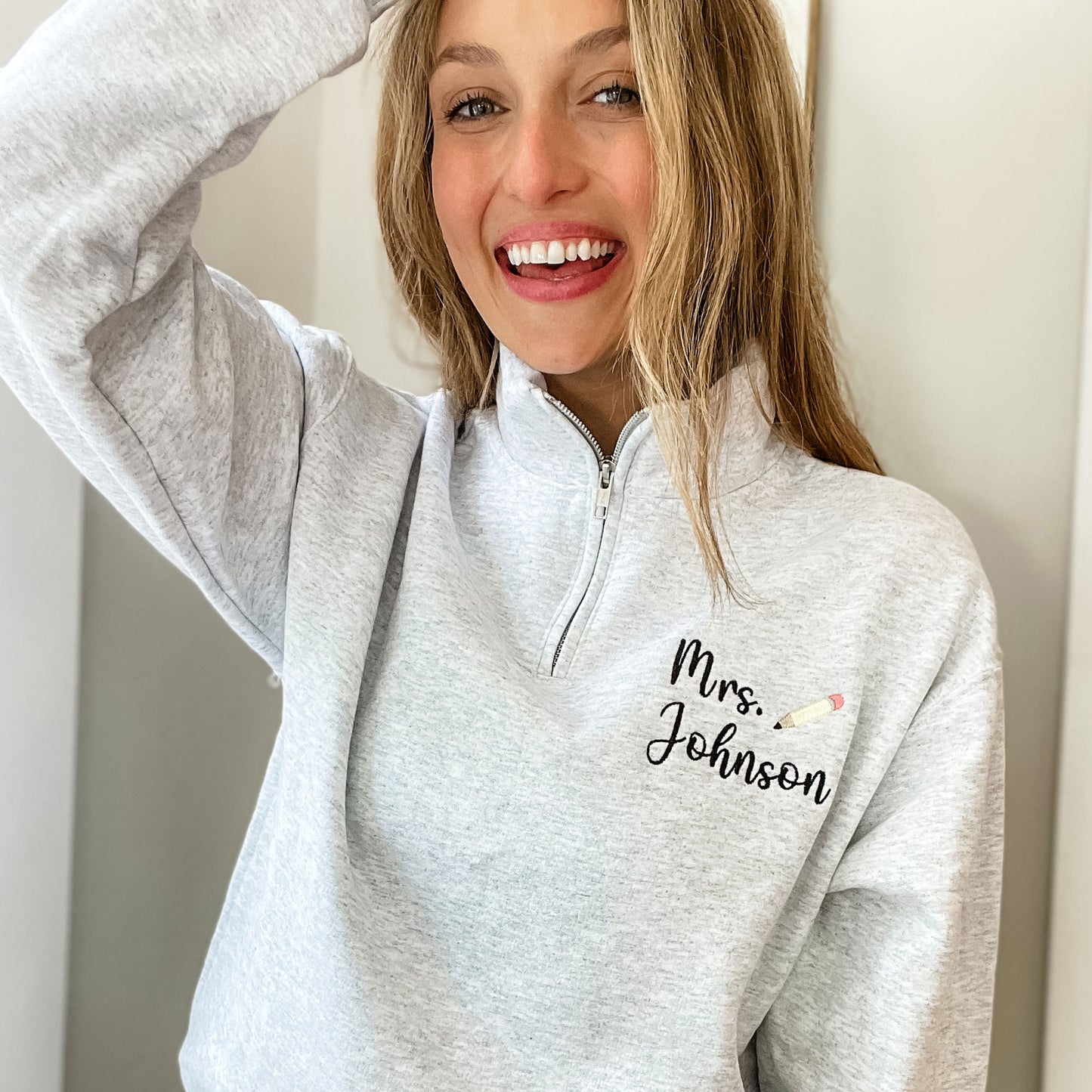woman wearing a light grey pullover sweatshirt with custom name and mini pencil embroidered design on the left chest
