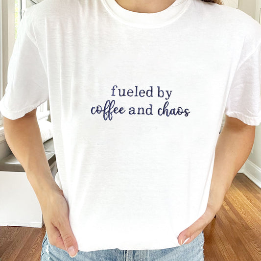 woman wearing a white comfort colors t-shirt with a custom embroidered fueled by coffee and chaos design in a dark purple thread