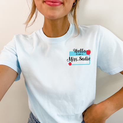 woman wearig a chambray blue comfort colors t-shirt with a custom name tag print on the left chest decorated with apples.