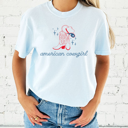 girl wearing an oversized chambray comfort colors t-shirt with a cute american cowgirl print in a rope font with cowgirl boots and a cowgirl hat