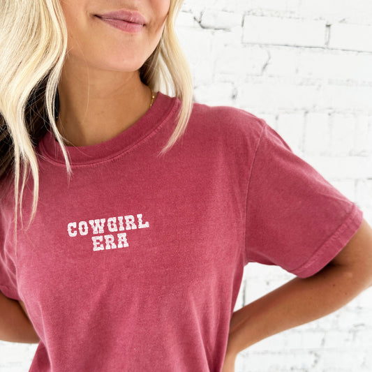 woman wearing a crimson comfort colors tee with a distressed cowgirl era printed design