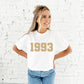 girl wearing a white comfort colors tee with a custom birth year printed design in a camel ink