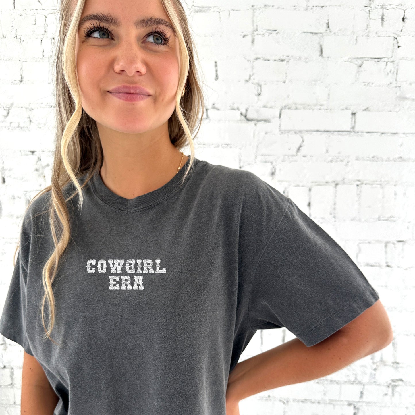 woman wearing a pepper comfort colors tee with a distressed cowgirl era printed design