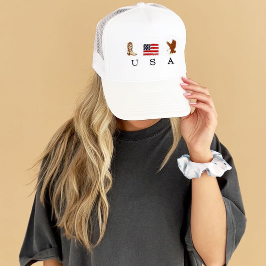 girl wearing a white trucker hat with a patriotic embroidered usa design featuring a cowboy boot, american flag, and bald eagle