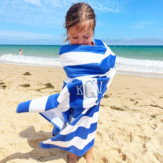 toddler girl on a beach wrapped in a royal blue and white stripped beach towel with KCV monogram embroidered in powder Blue thread