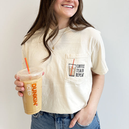young woman wearing an ivory comfort colors pocket t-shirt with iced coffee and coffee teach repeat embroidered design on the pocket holding a dunkin iced coffee