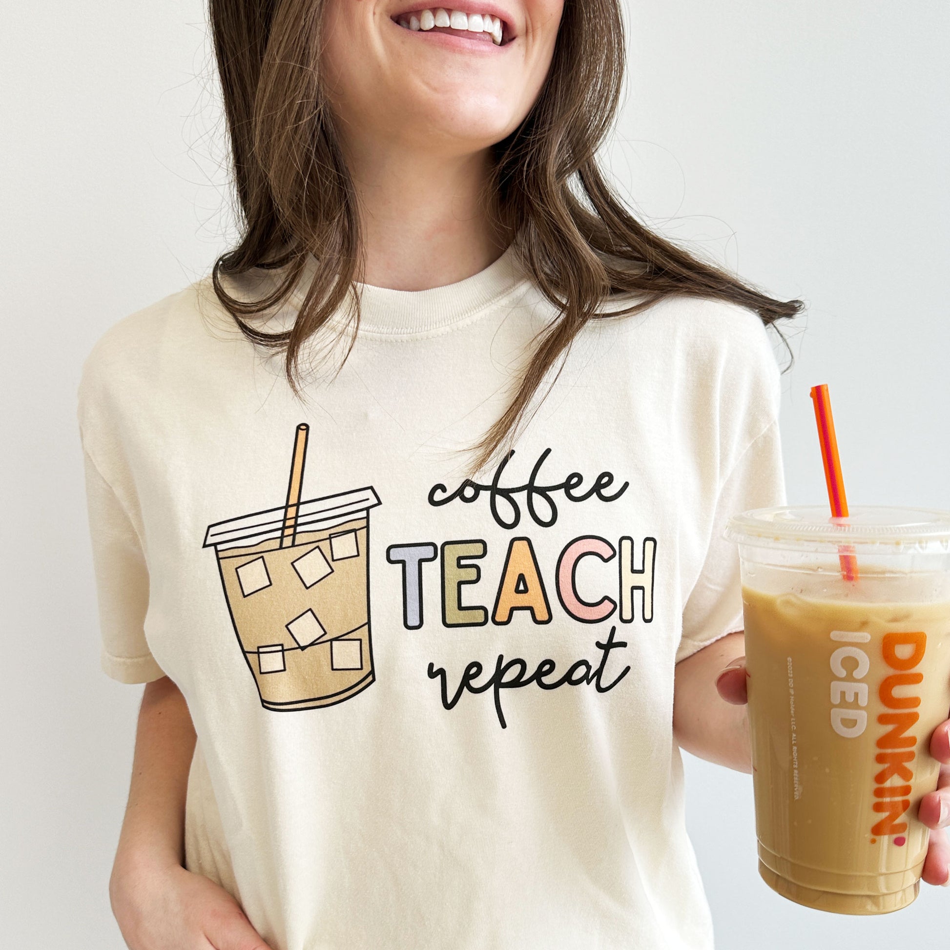 ivory comfort color crewneck t-shirt with printed design featuring a large iced coffee and the words: coffee teach repeat in a mixed font and multiple colors