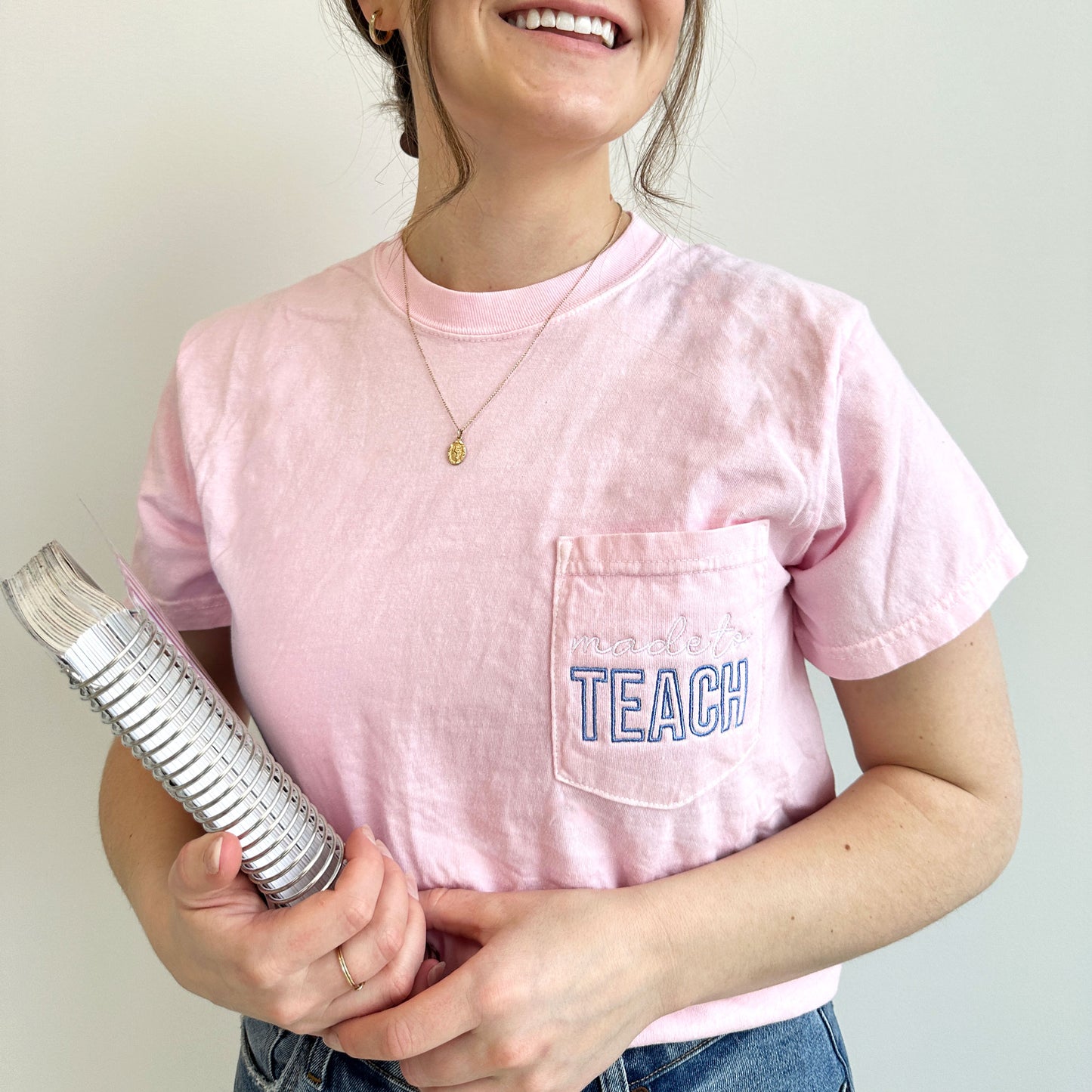 close up photo of a young woman wearing a blossom comfort colors t-shirt with made to teach embroidered design on the pocket in white and periwinkle threads