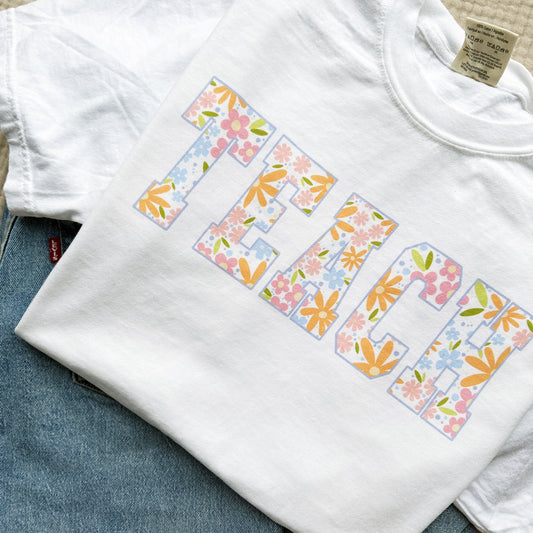cute white t-shirt with a large varsity font TEACH print with a colorful floral pattern fill