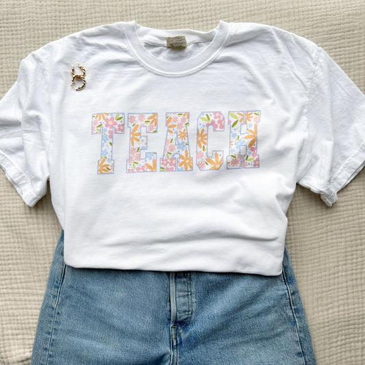 cute teacher outfit featuring blue jeans, a white comfort colors t-shirt with a colorful spring floral TEACH print