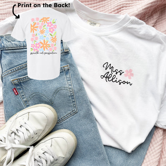white comfort colors tee with a playful floral print and growth not perfection in a script underneath on the back and a custom name and mini flower print on the front left chest