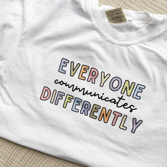 white comfort colors t-shirt with cute multi-color print reading everyone communicates differently in a mixed font