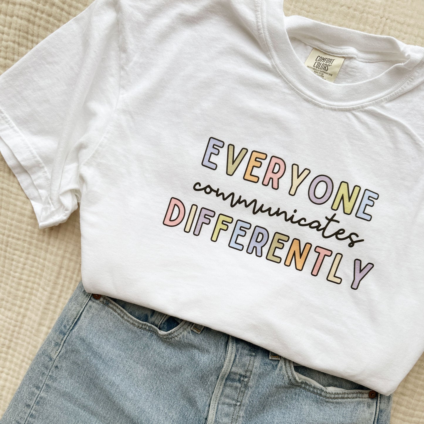 jeans and a white comfort colors crewneck short sleeve shirt with a colorful everyone communicates differently printed design