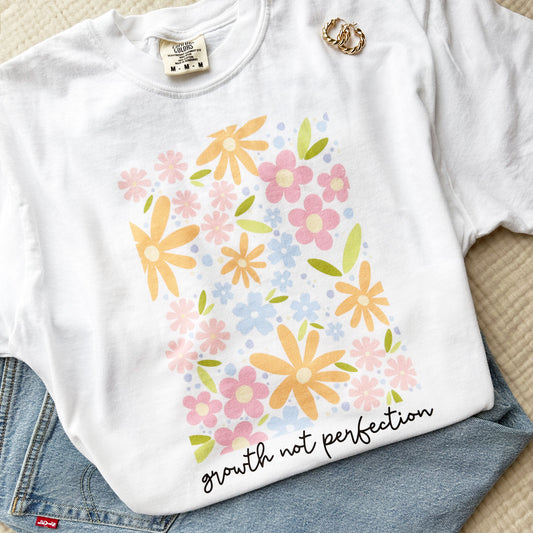 white comfort colors tee with a playful floral print and growth not perfection in a script underneath 