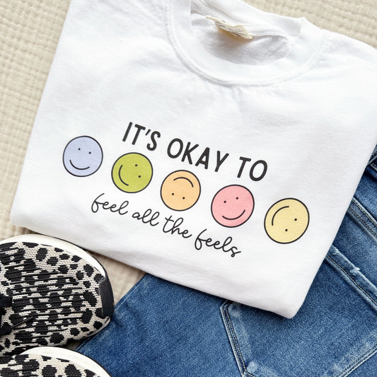 white school counselor tee with an it's okay to feel all the feels smiley face printed design