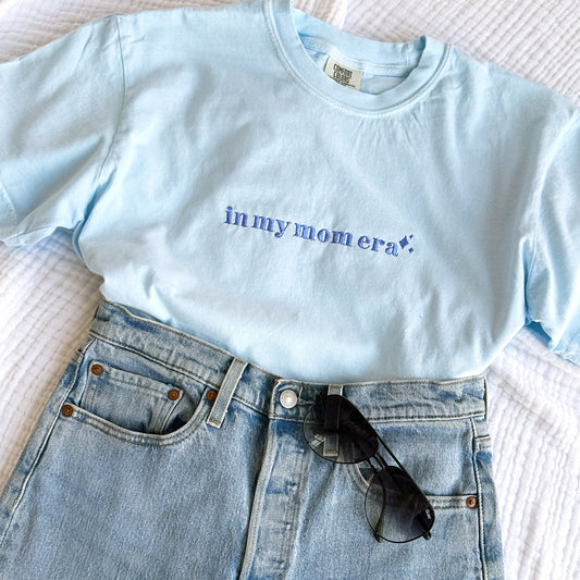 Chambray comfort colors t-shirt with embroidered in my mom era design across the chest in periwinkle thread styled with jeans and sunglasses