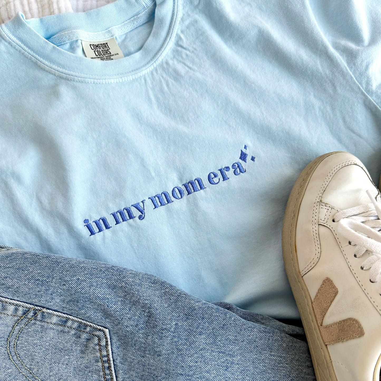 Chambray comfort colors t-shirt with embroidered in my mom era design across the chest in periwinkle thread styled with jeans and sneakers
