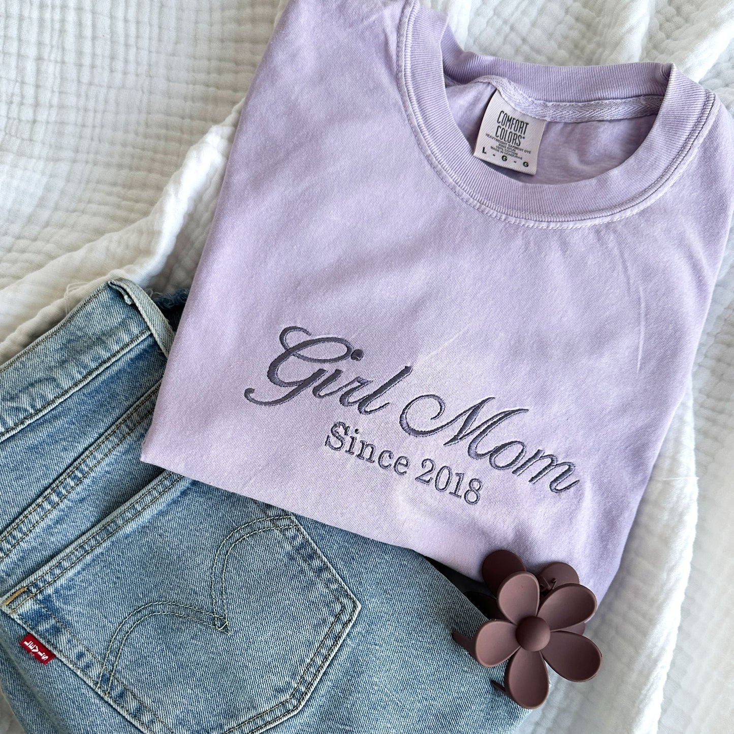 Orchid comfort colors t-shirt with embroidered Girl Mom since custom date design across the chest in smoky orchid thread. Styled with jeans and a flower hair clip