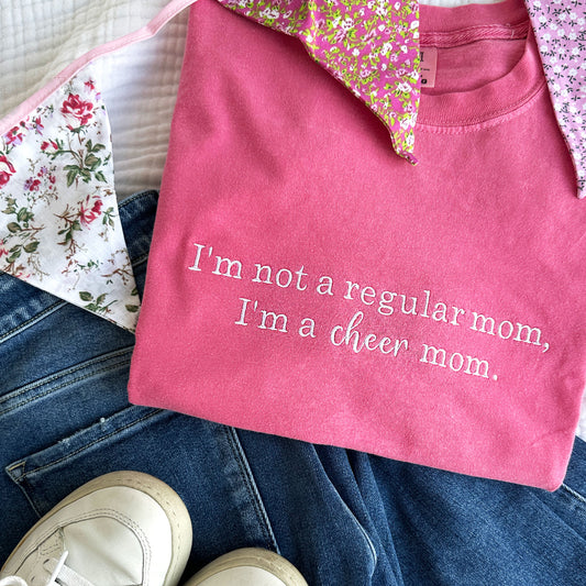 flat lay of a curnchberry comfort colors t-shirt with embroidered I'm not a regular mom, I'm a cheer mom design in white thread