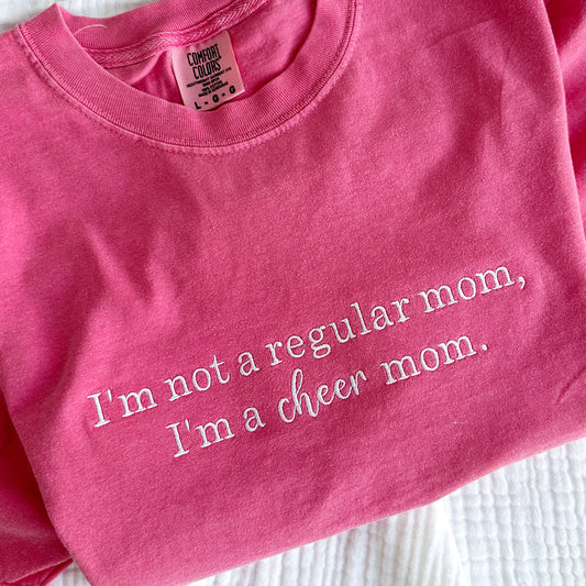 flat lay of a crunch berry pink comfort colors t-shirt with with embroidered  I'm not a regular mom, I'm a cheer mom design.