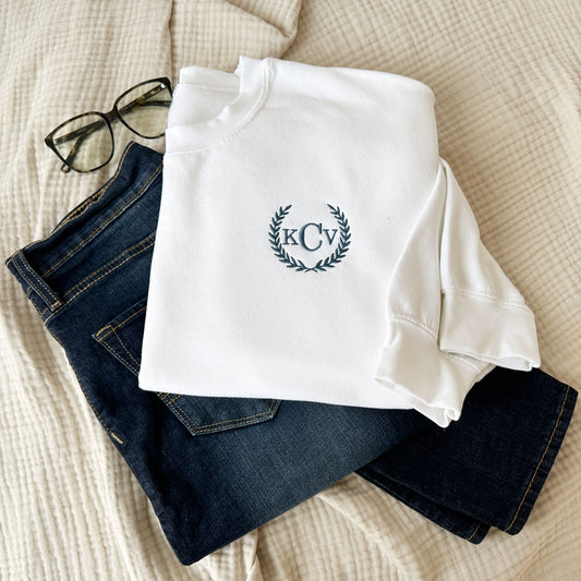 outfit layout featuring blue jeans and a white crewneck sweatshirt with a personalized laurel monogram embroidered design