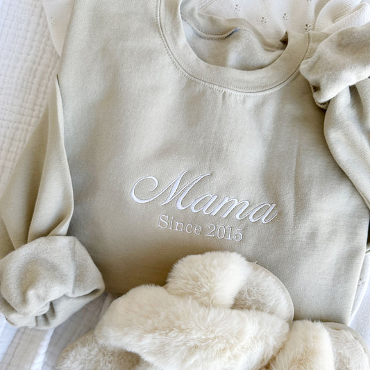 styled flat lay of a sand crewneck sweatshirt with embroidered Mama since customizable date in white thread across the chest