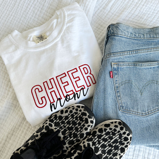 styled flat lay of a white comfort colors t-shirt with embroidered Cheer Mom design in black and red threads across the chest