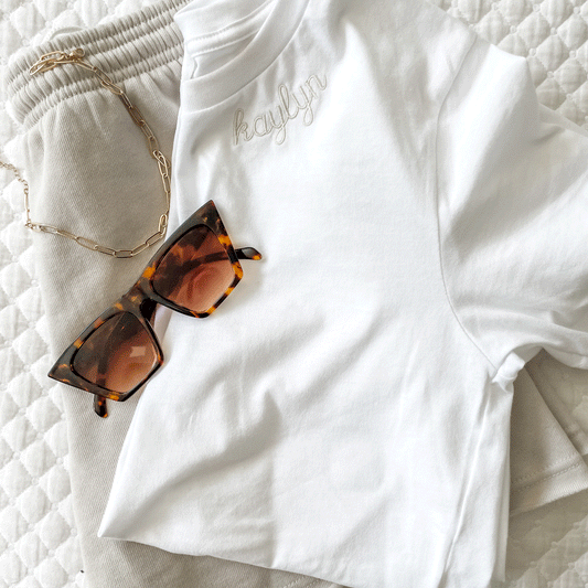flat lay of a white bella and canvas crewneck tee with kaylyn embroidered in natural thread along the neckline