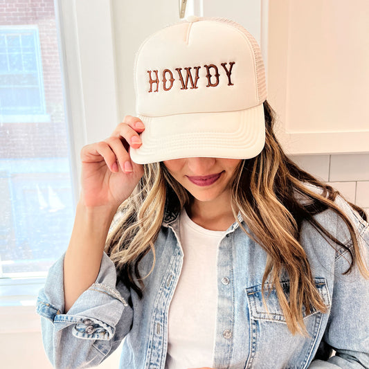 woman wearing a sand trucker hat with embroidered all caps howdy design in brown thread