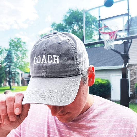 man standing on basketball court wearing a grey coach embroidered baseball hat