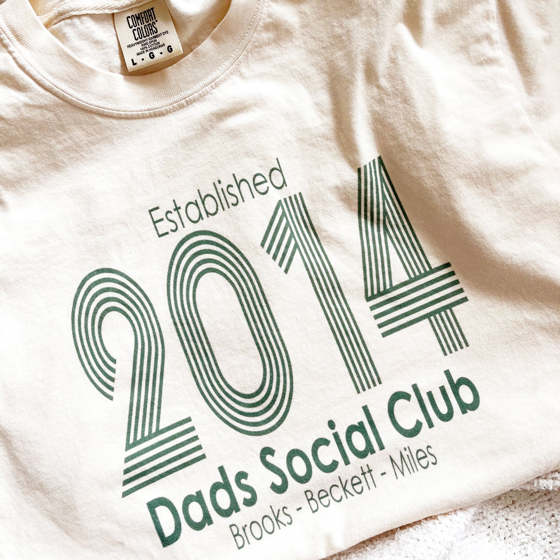 close up of a retro inspired printed design on a comfort colors t-shirt featuring a custom established date, dads social club, and kids names