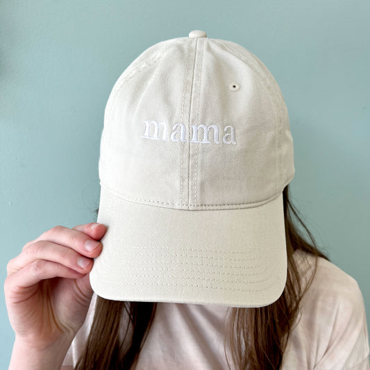 woman wearing a light khaki hat with custom mini mama embroidered design in a white thread.