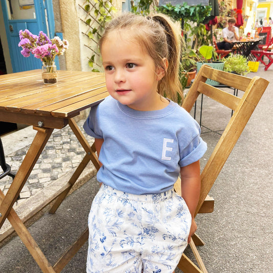 little girl wearing a washed denim comfort colors t-shirt with her initial embroidered in a block font 