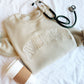 coffee cup, stethoscope, and sand crewneck sweatshirt with NURSE embroidered across the chest in neutral thread colors