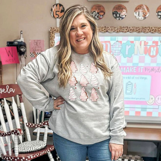 teacher standing in her classroom wearing an athletic heather sweatshirt with  a pink little debbie christmas tree design on the front.
