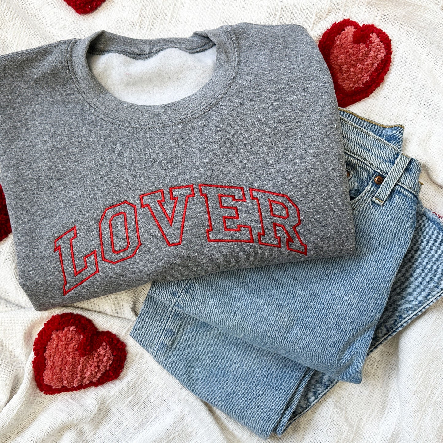 jeans and a dark gray crewneck sweatshirt with LOVER embroidered in a red thread across the chest